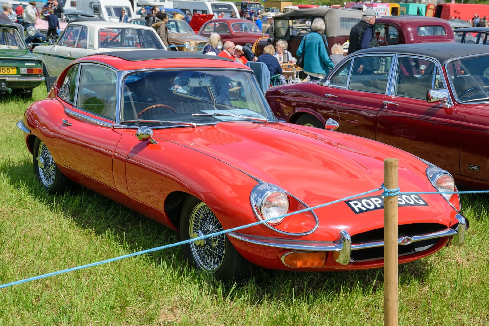 A red 1969 Jaguar E-Type Series 2 coupe on grass at a classic car show, front three-quarter view, UK registration ROP 750G