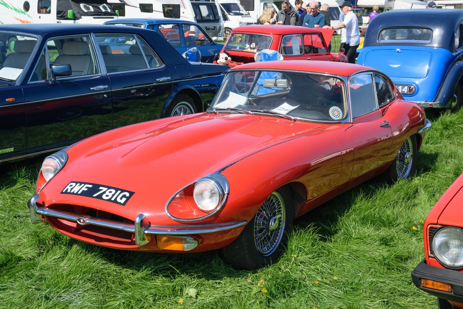 A red 1969 Jaguar E-Type Series 2 coupe on grass among other classics, front three-quarter view, UK registration RWF 781G