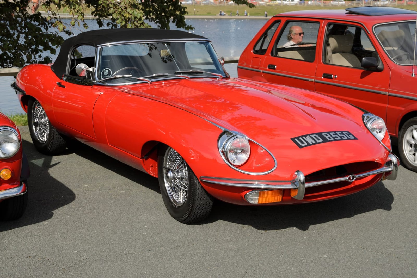 A red 1969 Jaguar E-Type Series 2 roadster parked by a lake, front three-quarter view, UK registration UWD 855G