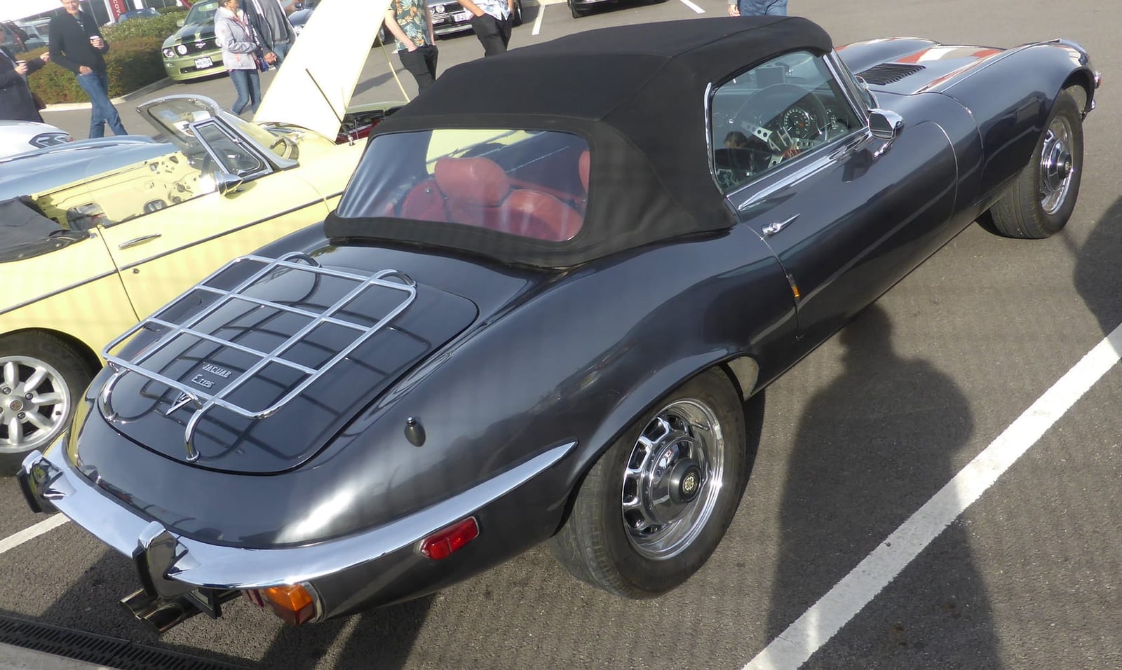 The rear view of a black 1973 Jaguar E-Type Series 3 V12 roadster with a luggage rack, showing four exhaust tips