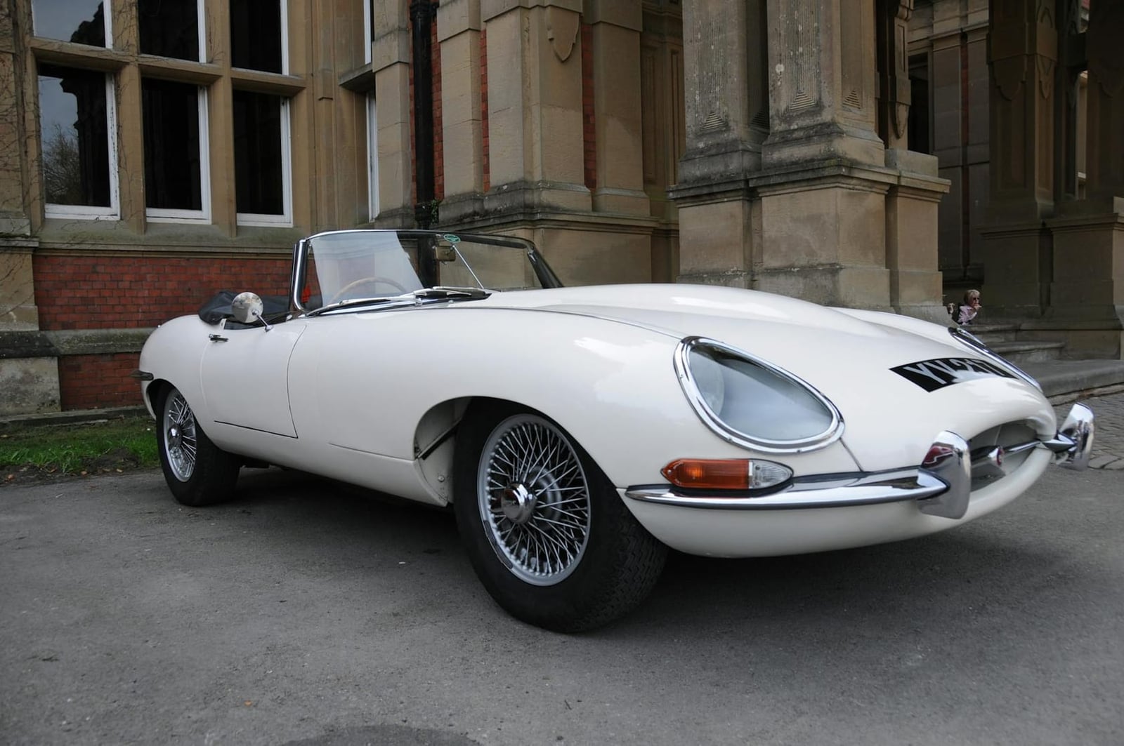A white Jaguar E-Type roadster parked beside historic buildings
