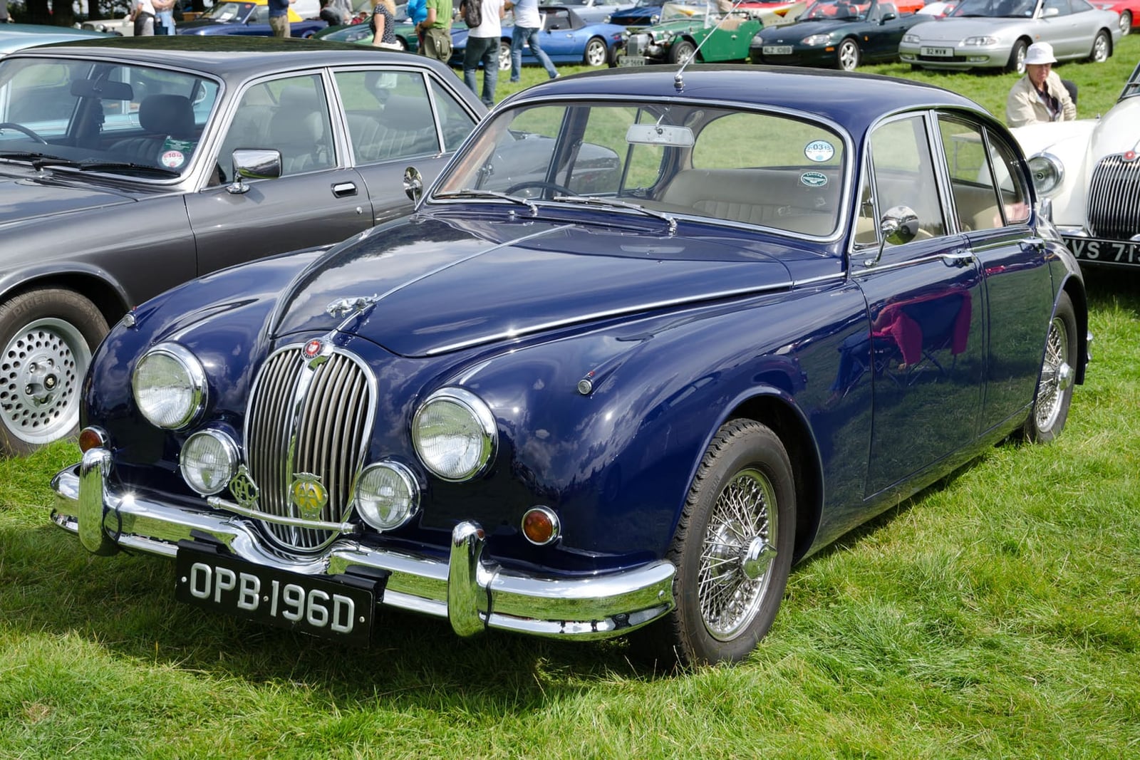 A dark blue 1966 Jaguar Mk2 2.4 with a UK registration parked on grass at a show