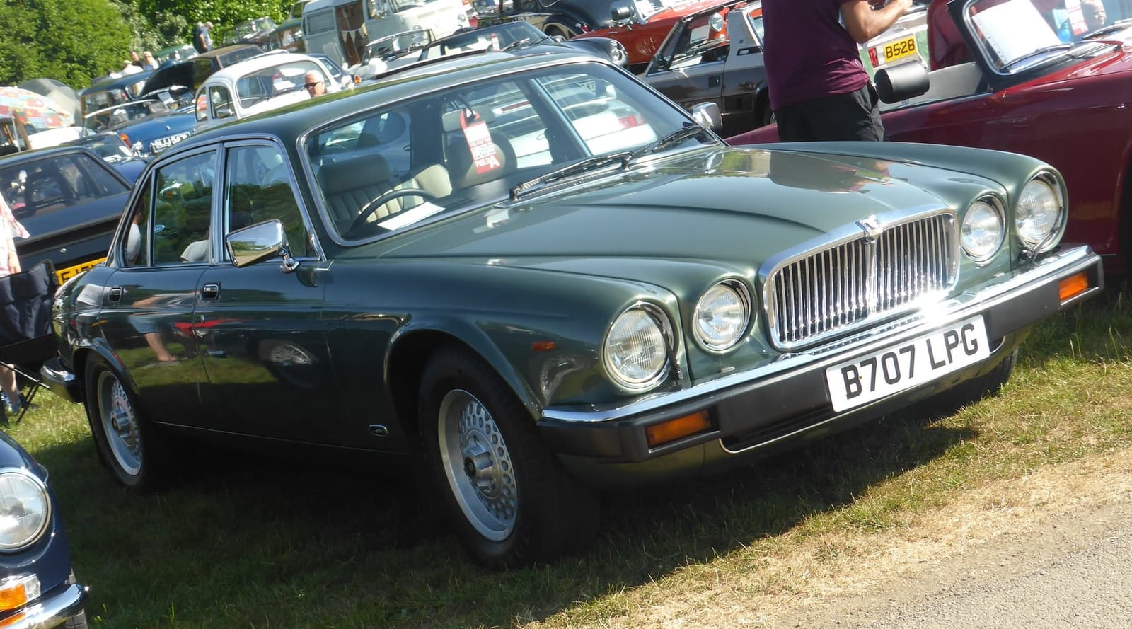The rusted bare shell of a maroon Jaguar XJ Series 3 propped against a fence