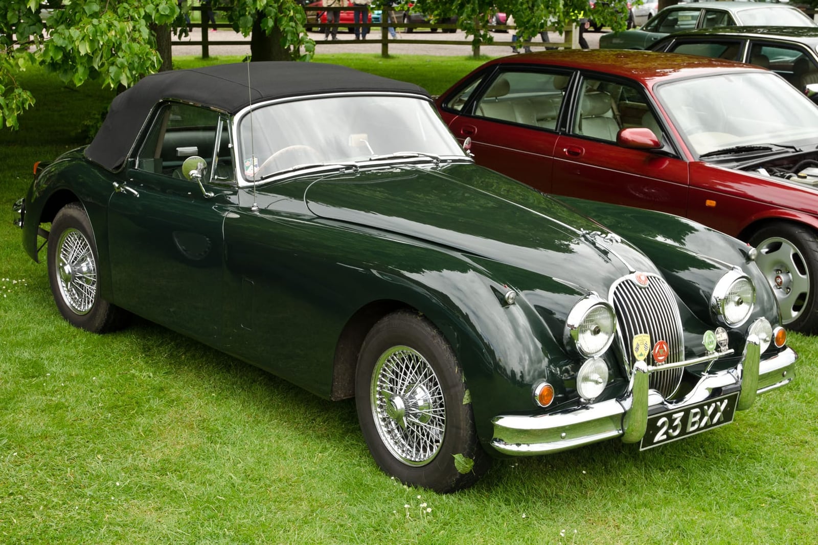 A dark green 1961 Jaguar XK150 3.4 drophead coupé with a UK registration on a show field, a Jaguar saloon behind