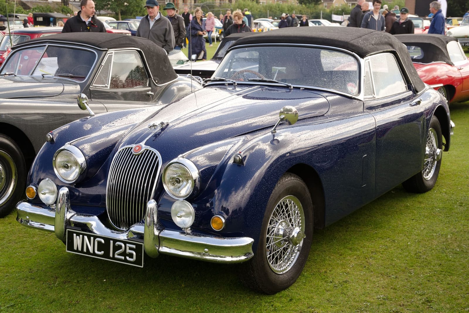 A dark blue 1958 Jaguar XK150 drophead coupé with its hood up and a UK registration on a show field
