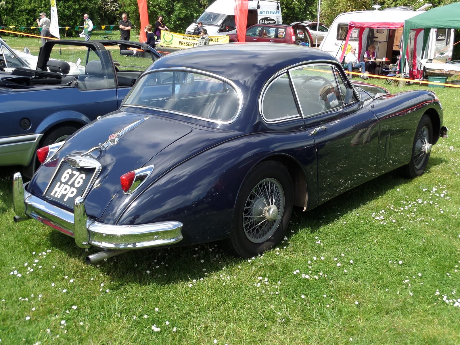 The rear of a dark blue Jaguar XK150 fixed-head coupé with a UK registration on grass at a show
