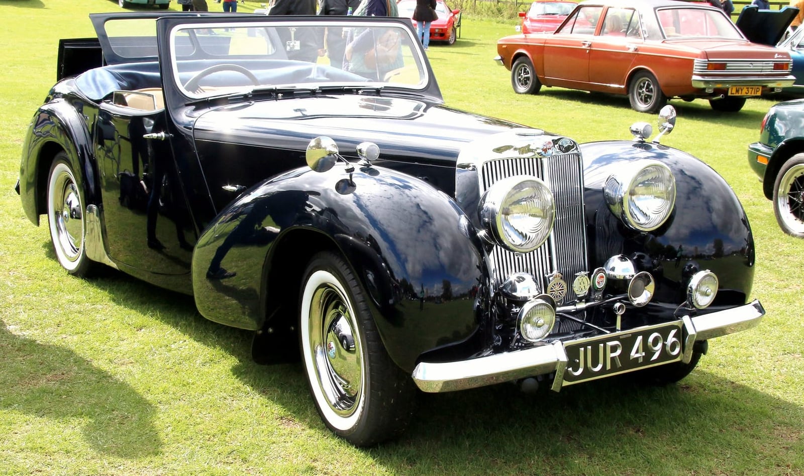 A black 1948 Triumph 1800 Roadster on grass at a classic car show, front three-quarter view, UK registration JUR 496