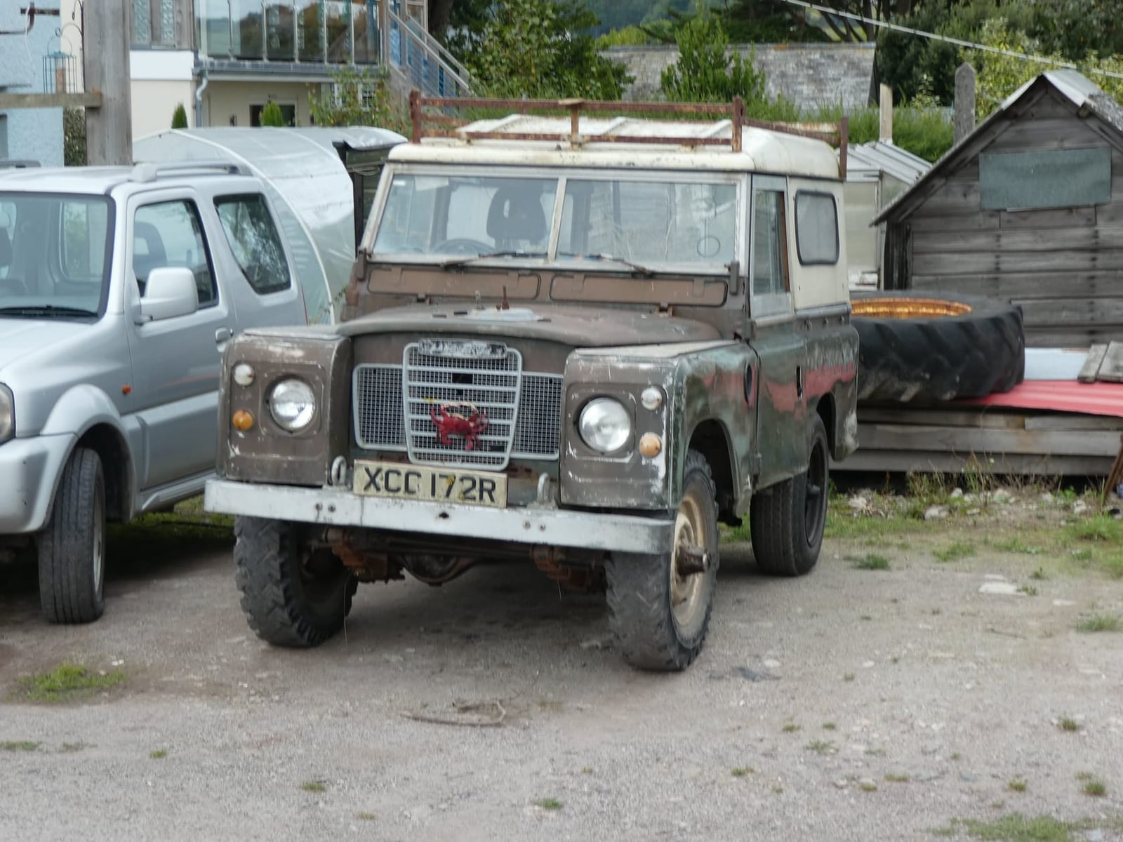 An unrestored green 1977 Land Rover Series III 88 diesel with a UK registration parked on gravel