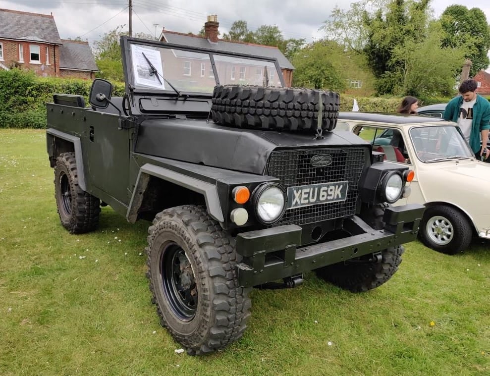 A green 1972 Land Rover Lightweight with spare wheels mounted on the bonnet at a vehicle show, UK registration XEU 69K