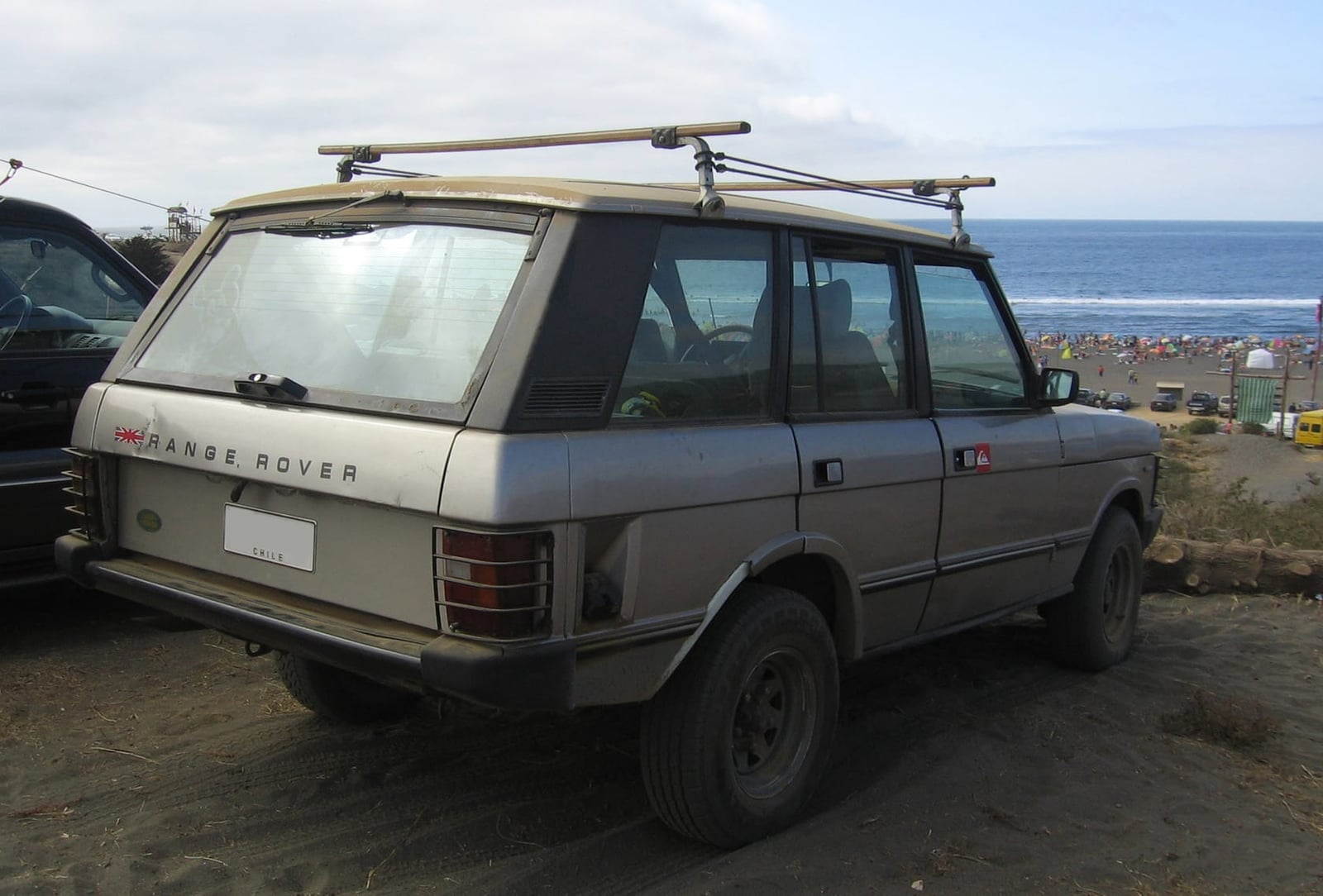 The rear of a grey 1985 Range Rover Vogue with a roof rack parked on a beach