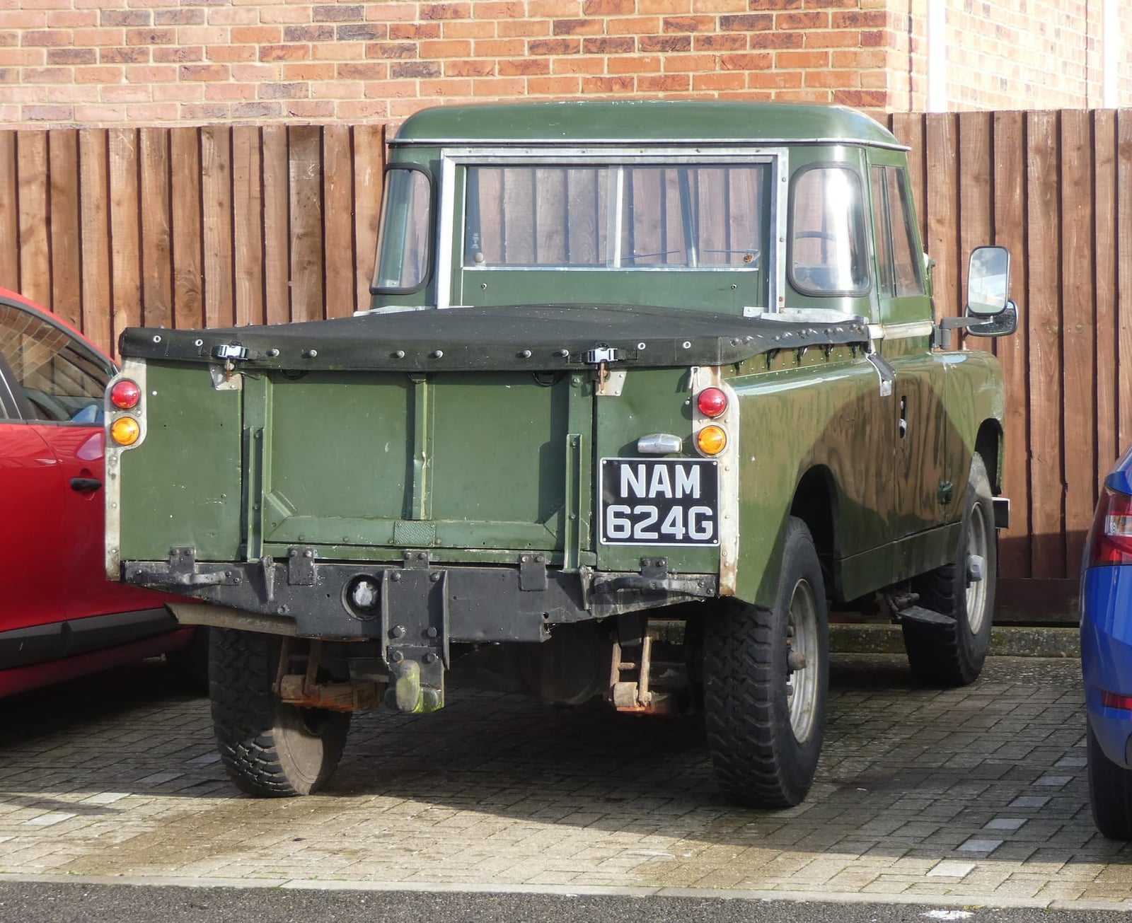 A green 1968 Land Rover Series IIA 109 pick-up with a UK registration parked against a fence