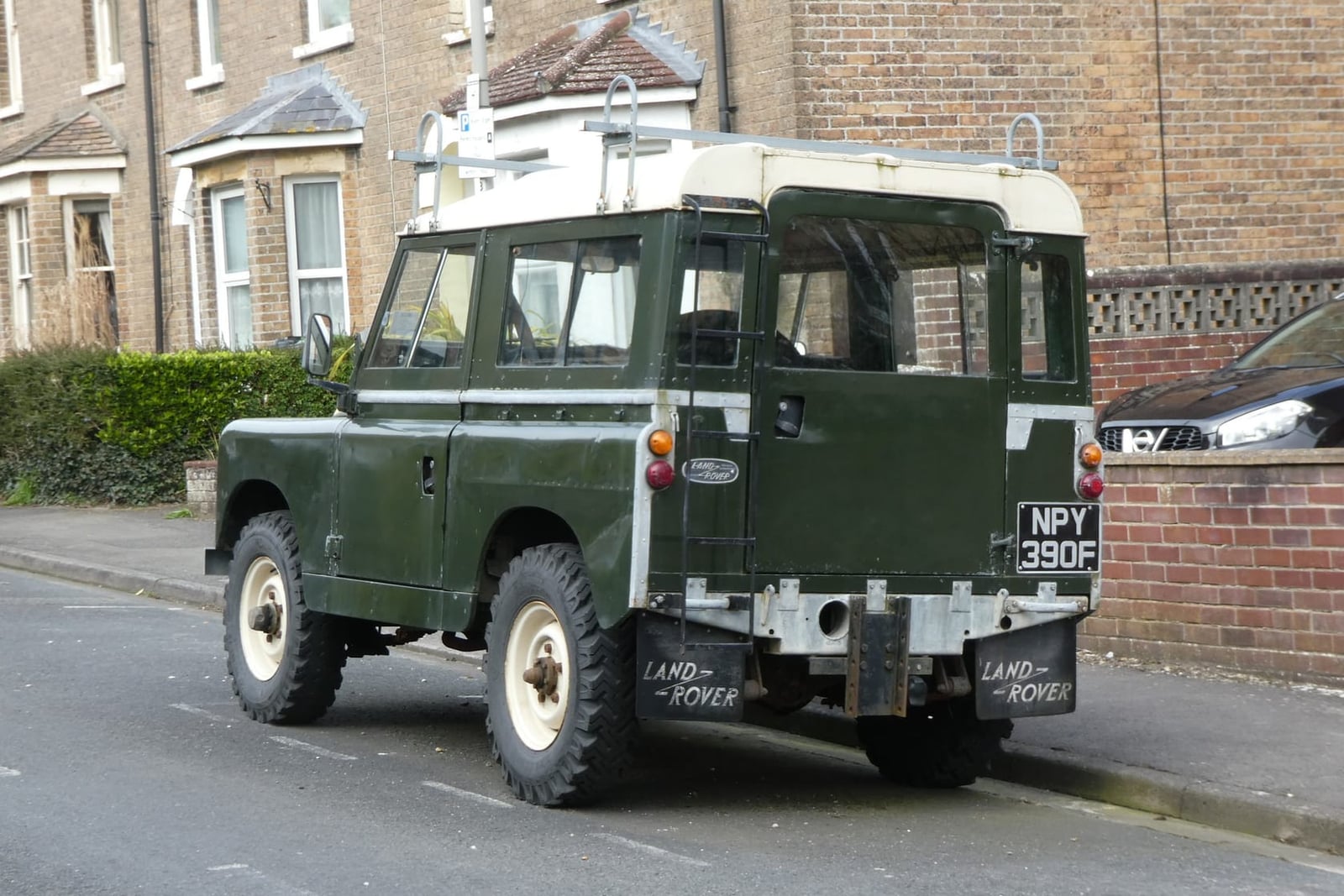 A dark green 1968 Land Rover Series IIA 88 station wagon with a white roof and a UK registration in a residential street