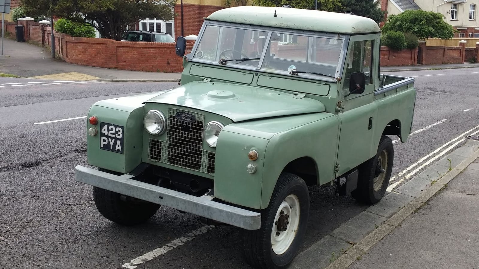 A pale green 1962 Land Rover Series IIA 88 pick-up with a UK registration parked in a suburban street