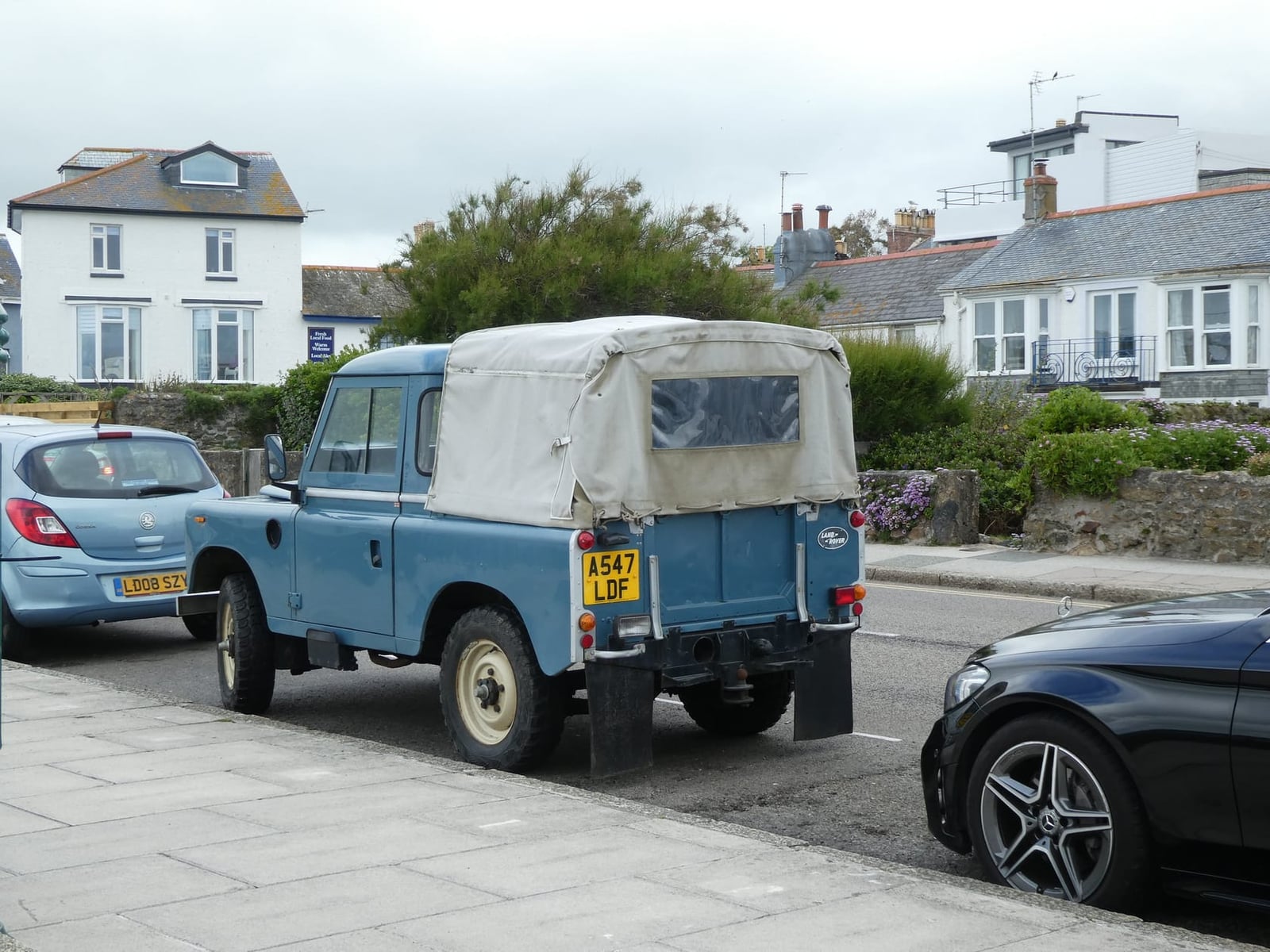 A blue 1984 Land Rover Series III 88 with a canvas tilt and a UK registration parked in a seaside street