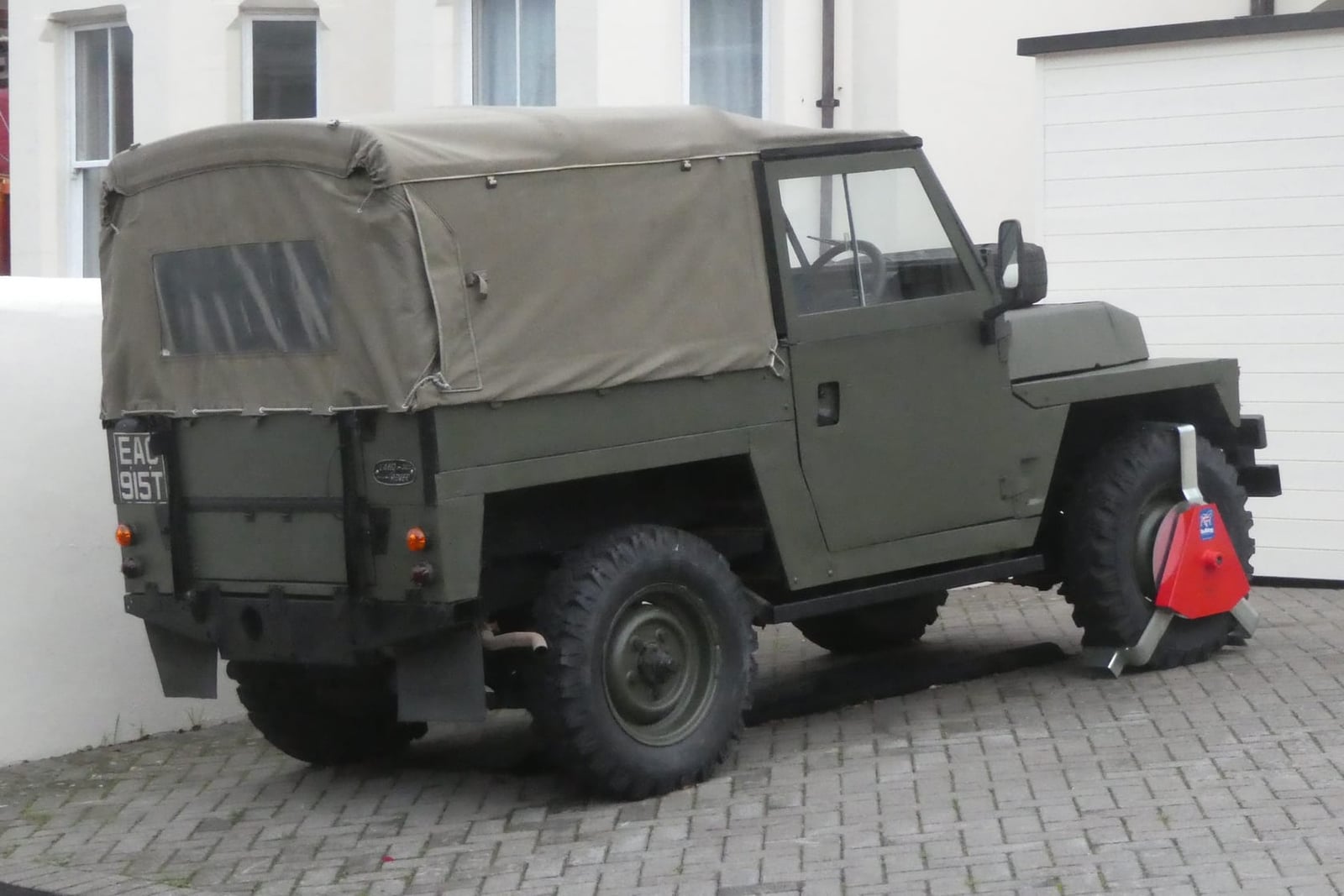 An olive green ex-military 1972 Land Rover Series III Lightweight with canvas top parked on a street