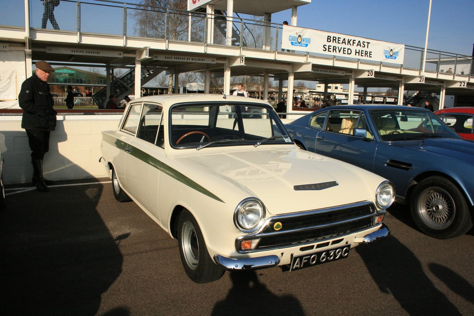 A white Lotus Cortina with green flash at the Goodwood circuit, other classics behind