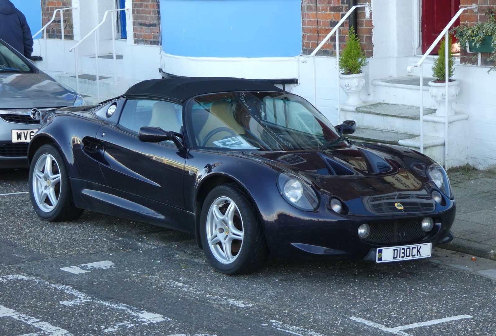 A dark blue 1998 Lotus Elise S1 parked on a street with its hood up and a UK registration