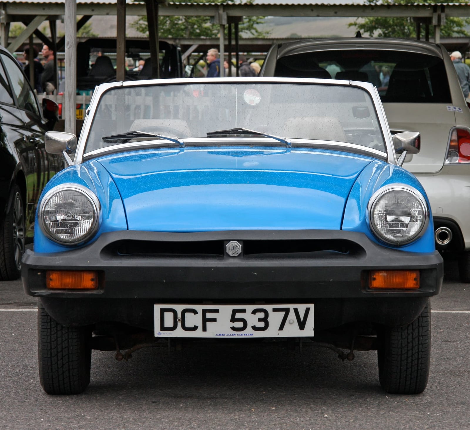 A blue MG Midget 1500 with black rubber bumpers and a UK registration parked at a show
