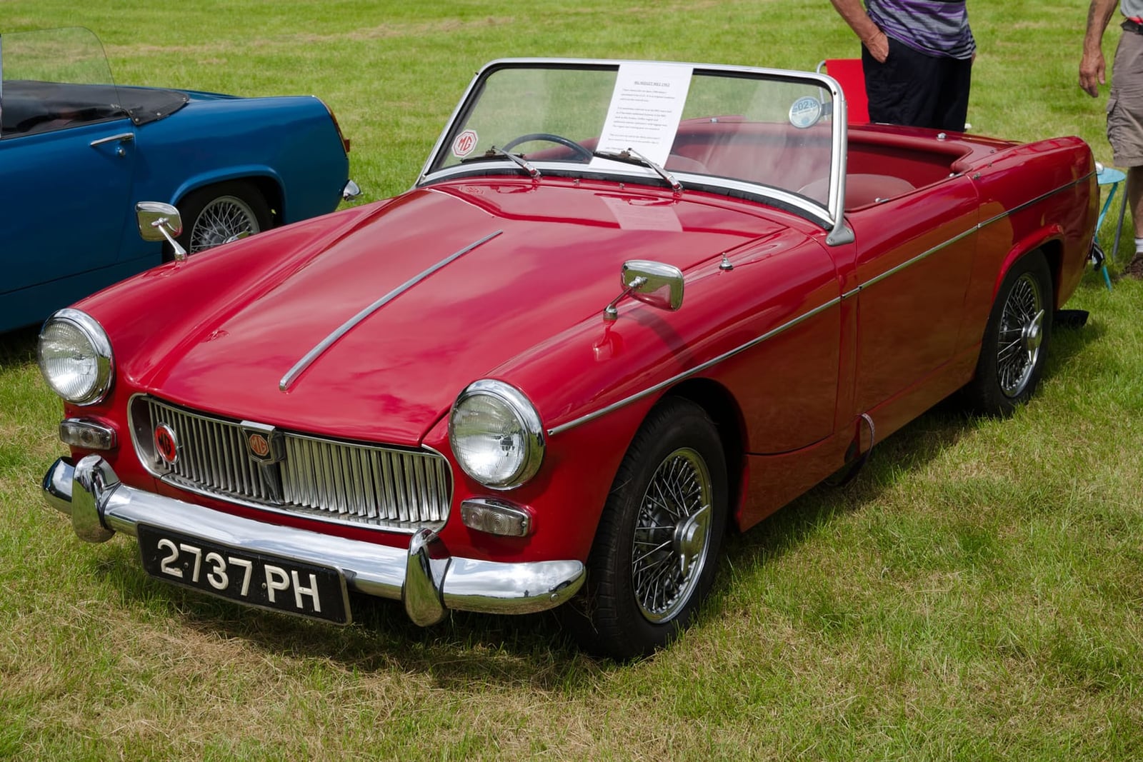 A red 1963 MG Midget Mk I with wire wheels and a UK registration on a show field