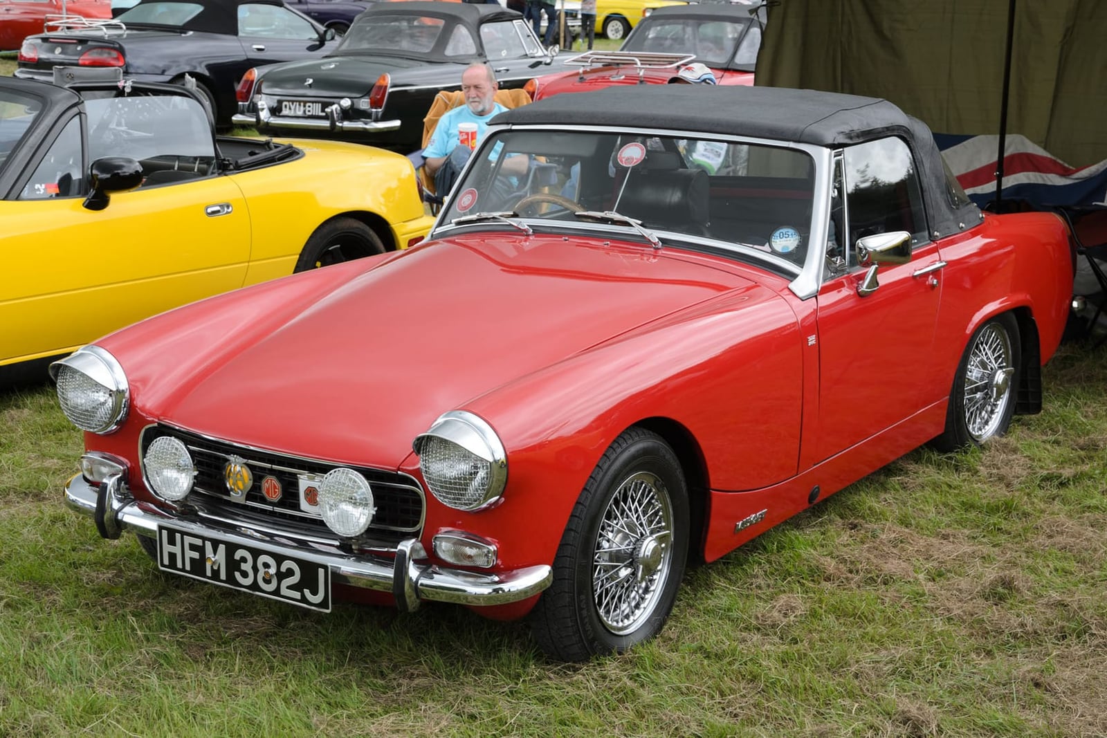 A red 1970 MG Midget Mk III with a black hardtop and a UK registration on grass at a show