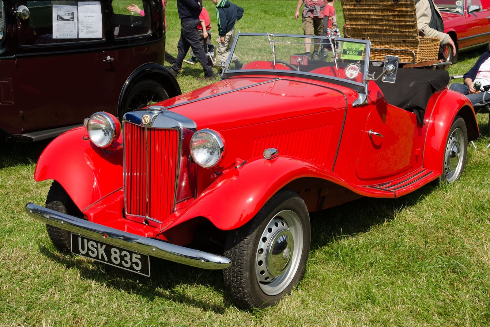 A red 1952 MG TD with a UK registration and disc wheels on a show field