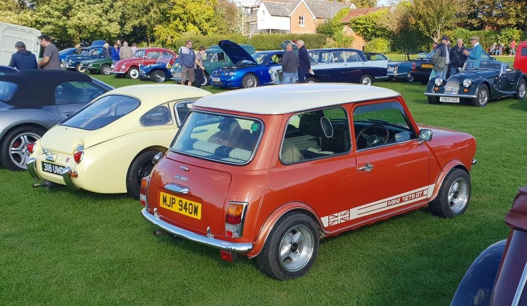 An orange Mini 1275GT with a white roof, rear three-quarter view