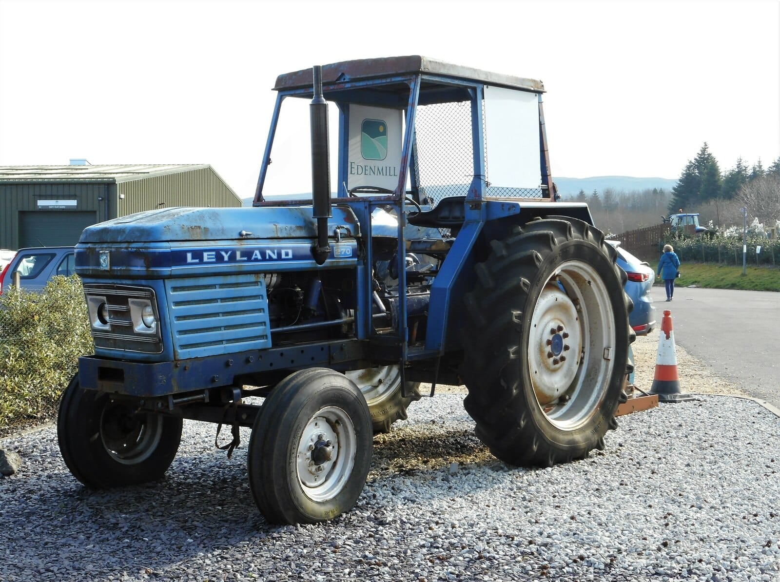 A blue Leyland 270 tractor with a safety cab, badged Leyland on the grille, parked on gravel at a farm shop