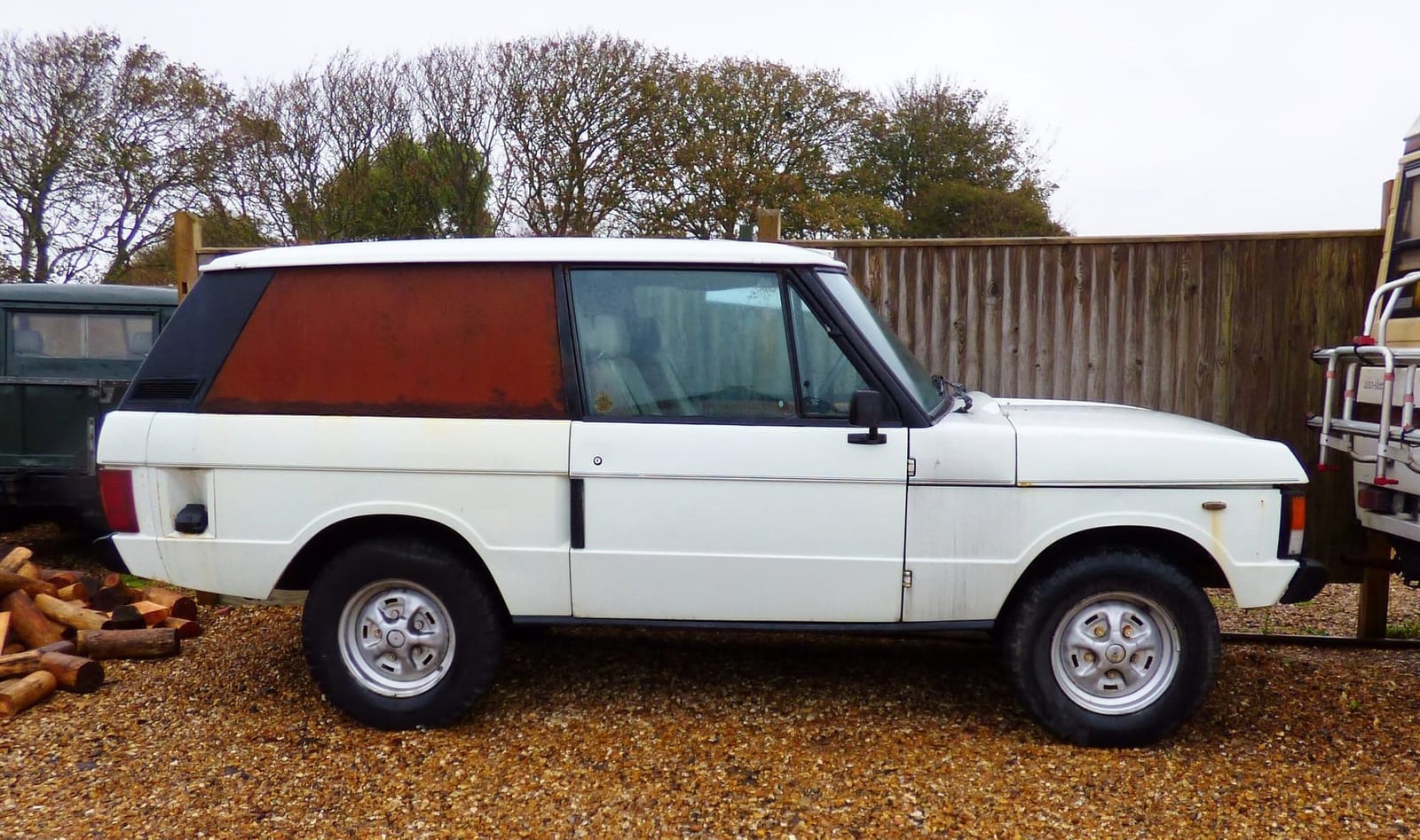 A two-door Range Rover Classic in white and orange primer under restoration in a yard