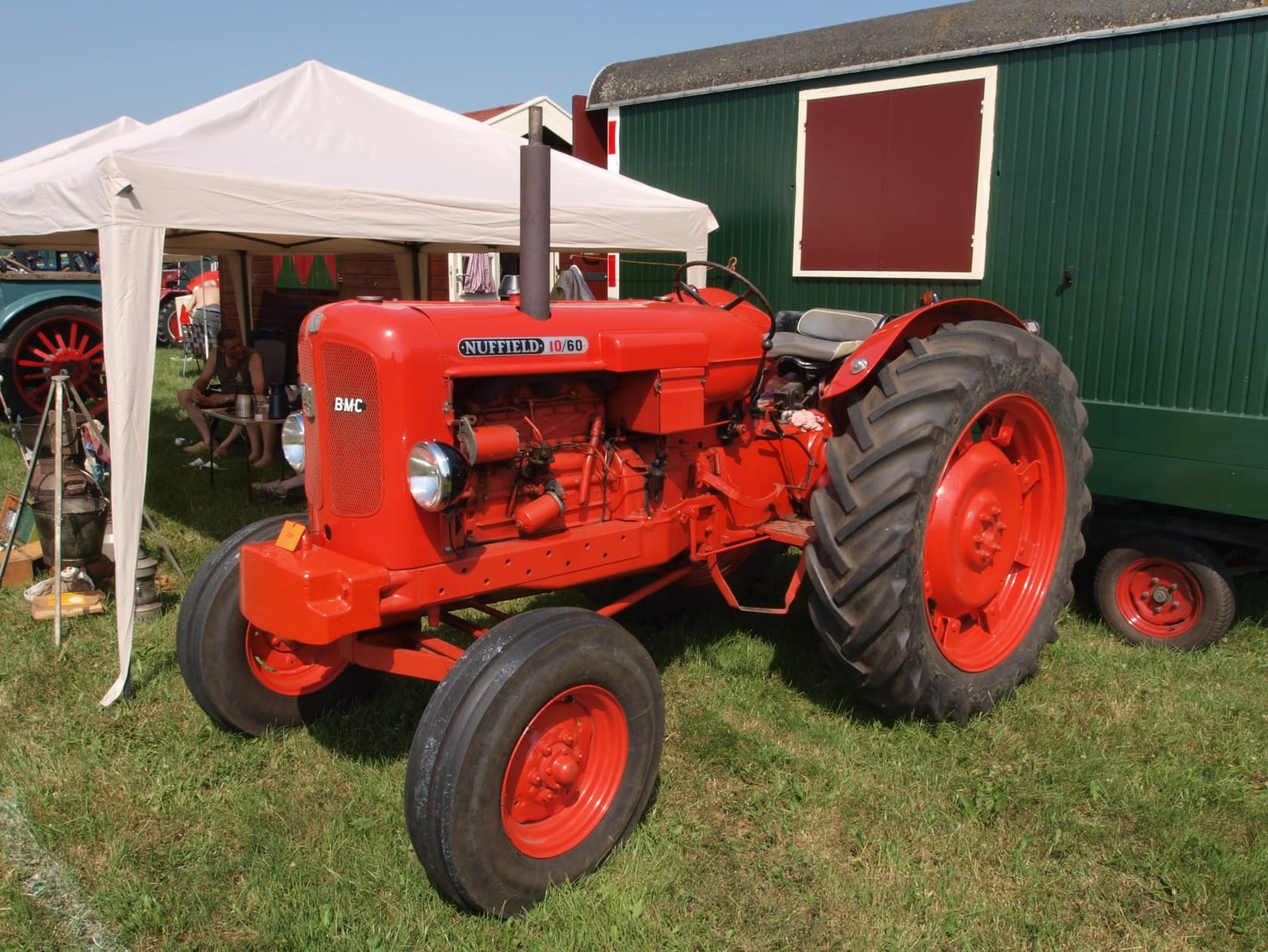 An orange Nuffield 10/60 with a BMC badge, front three-quarter view at a show beside a green wagon