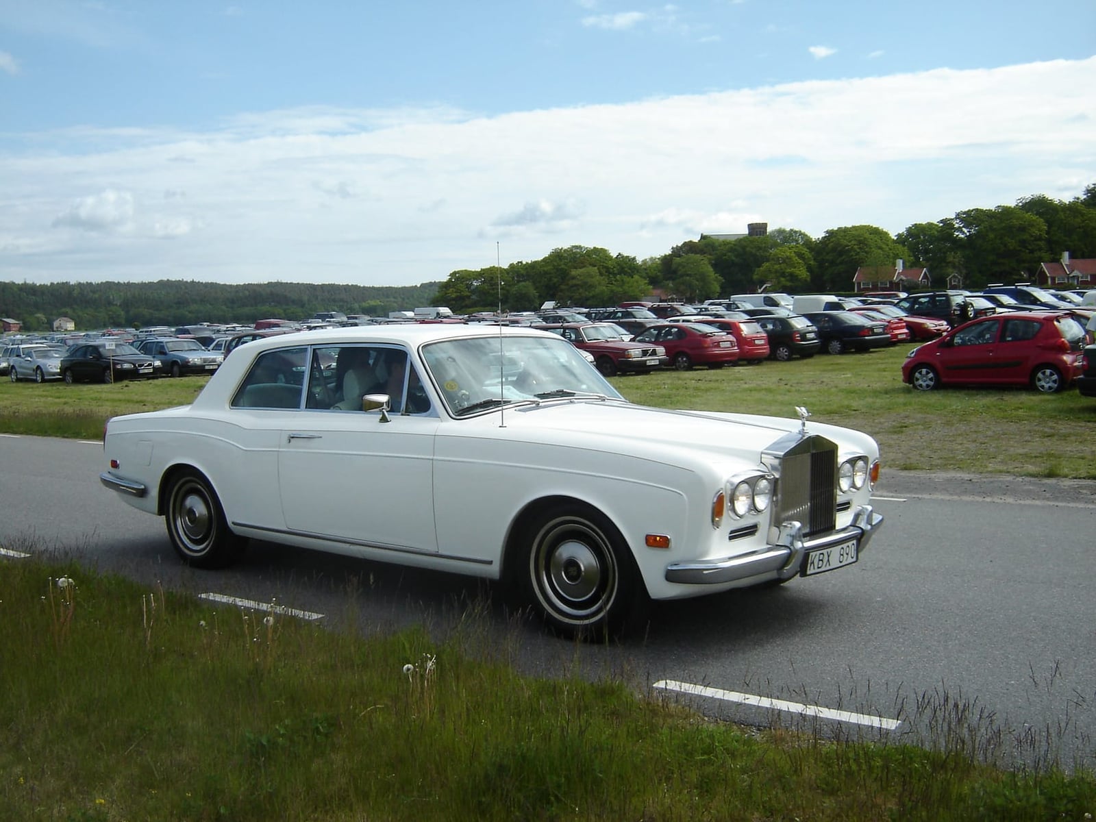 A white Rolls-Royce Corniche fixed-head coupe parked by a show field
