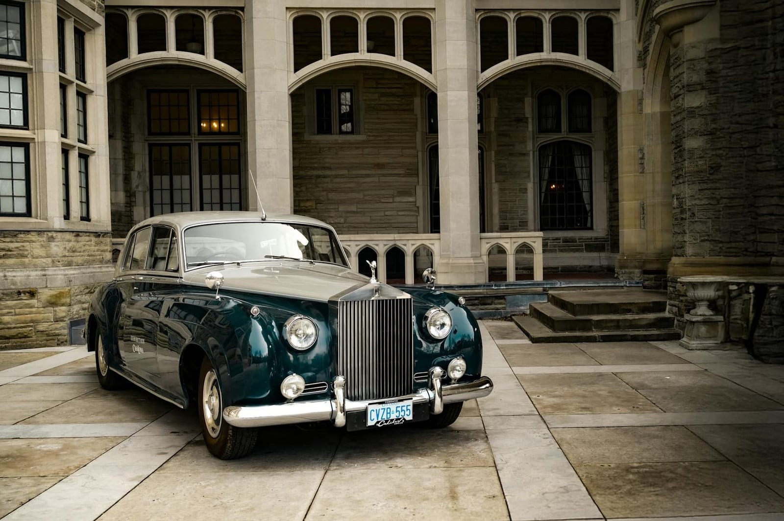 A green and grey Rolls-Royce Silver Cloud parked in a mansion courtyard