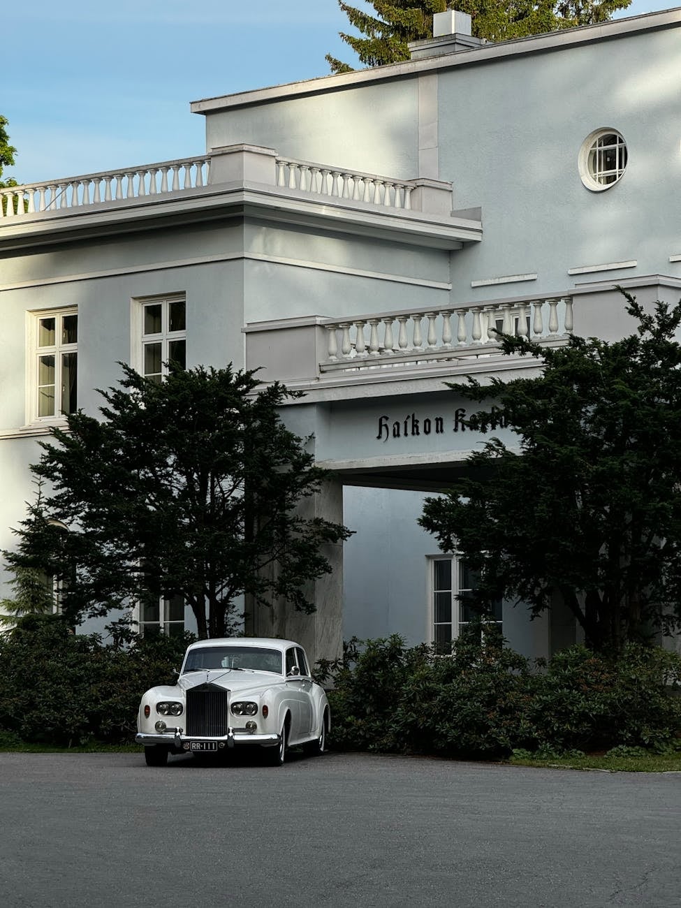 A white Rolls-Royce Silver Cloud parked in front of a white villa