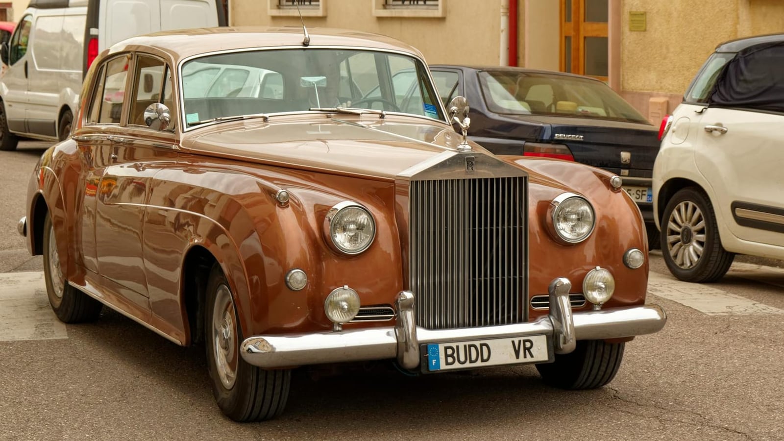 A brown and cream Rolls-Royce Silver Cloud parked on a narrow street