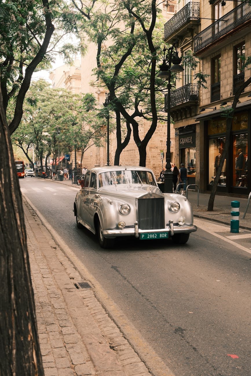 A cream Rolls-Royce Silver Cloud on a tree-lined city street