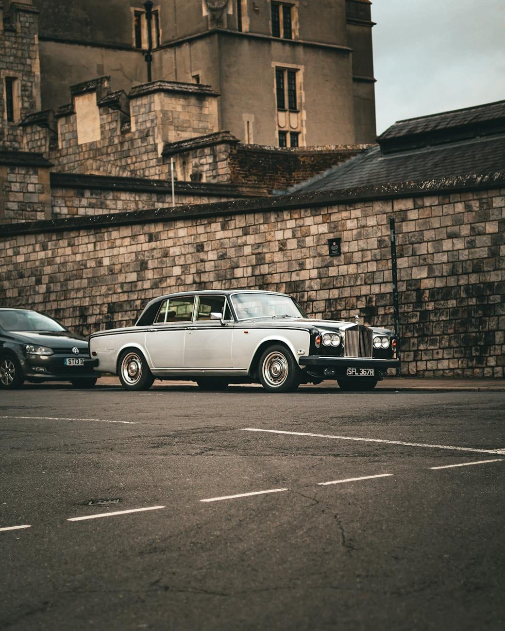 A white Rolls-Royce Silver Shadow parked beneath a castle wall
