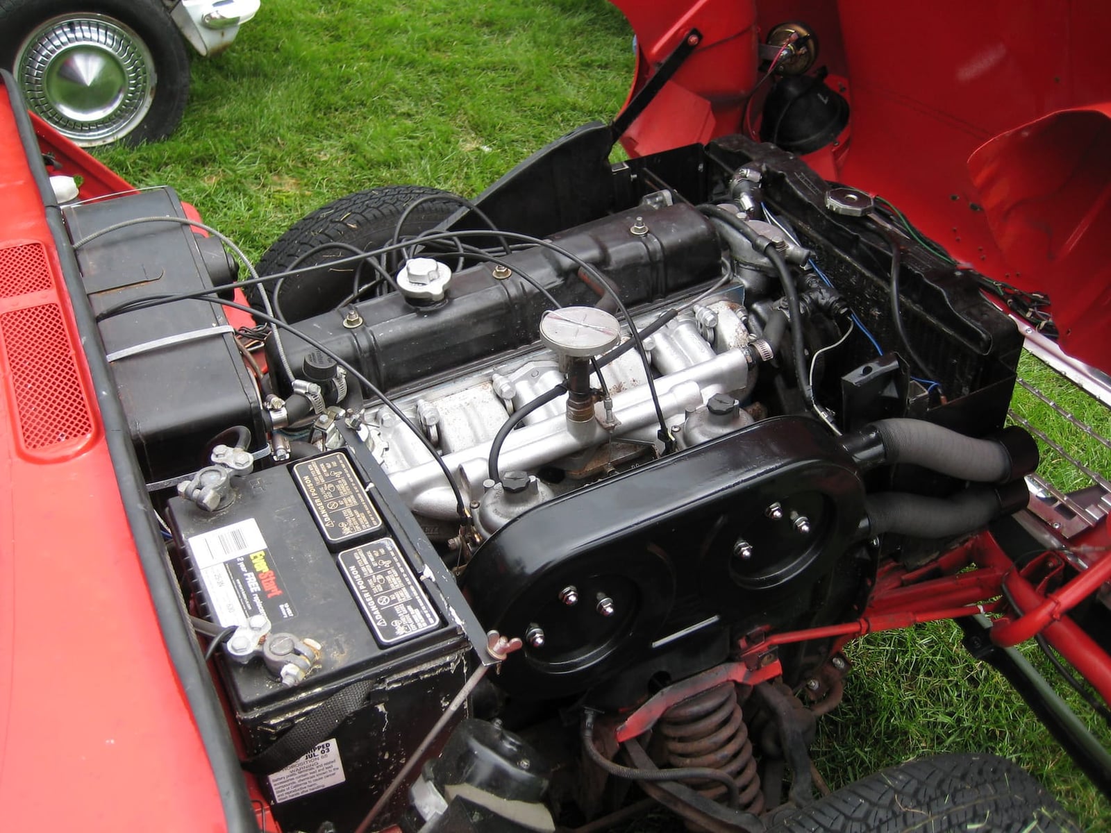 The engine bay of a Triumph Vitesse with the whole front end tilted forward, showing the six-cylinder engine and front suspension
