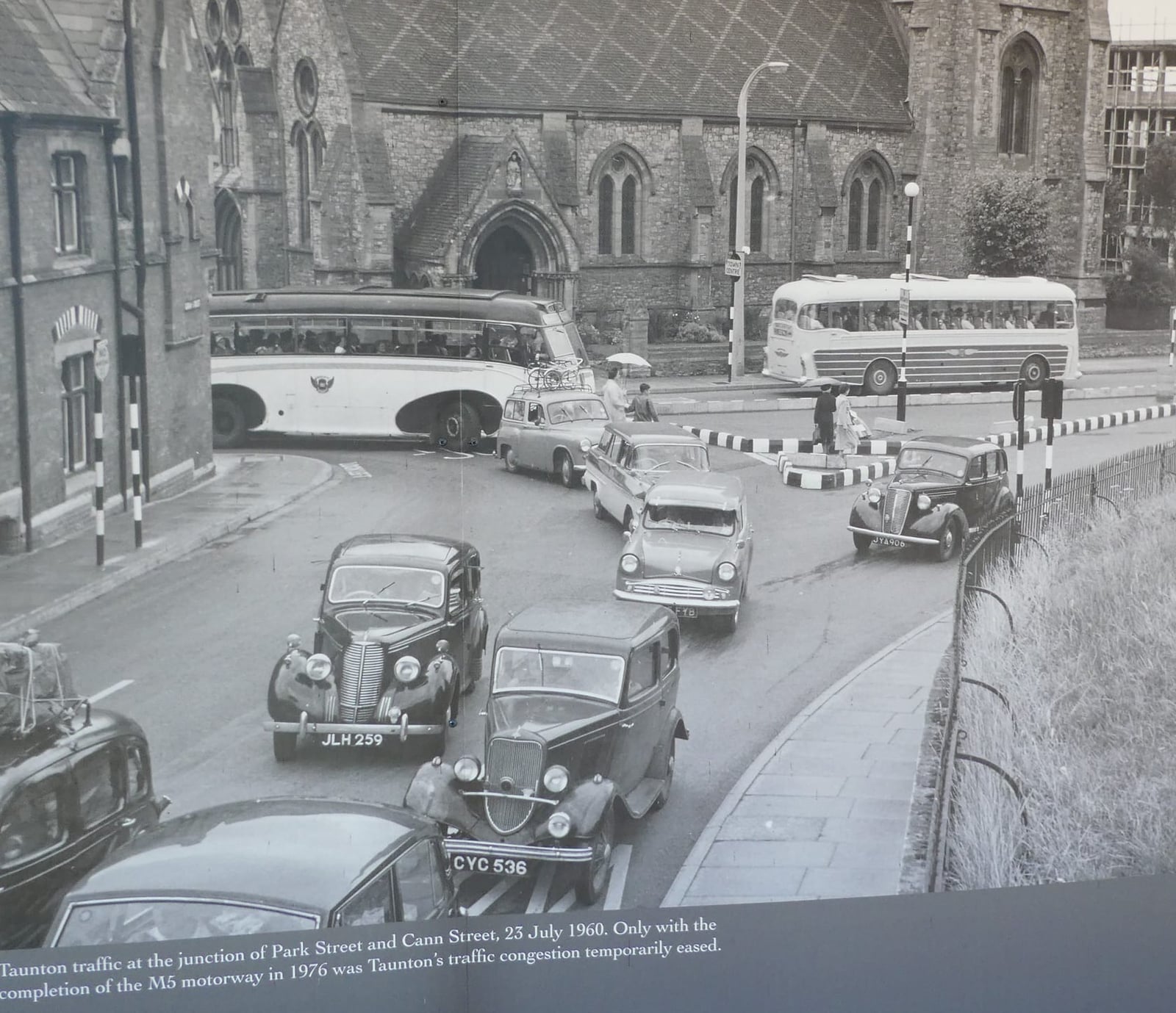 A black and white photograph of traffic in Taunton in 1960 including a razor-edge Triumph saloon