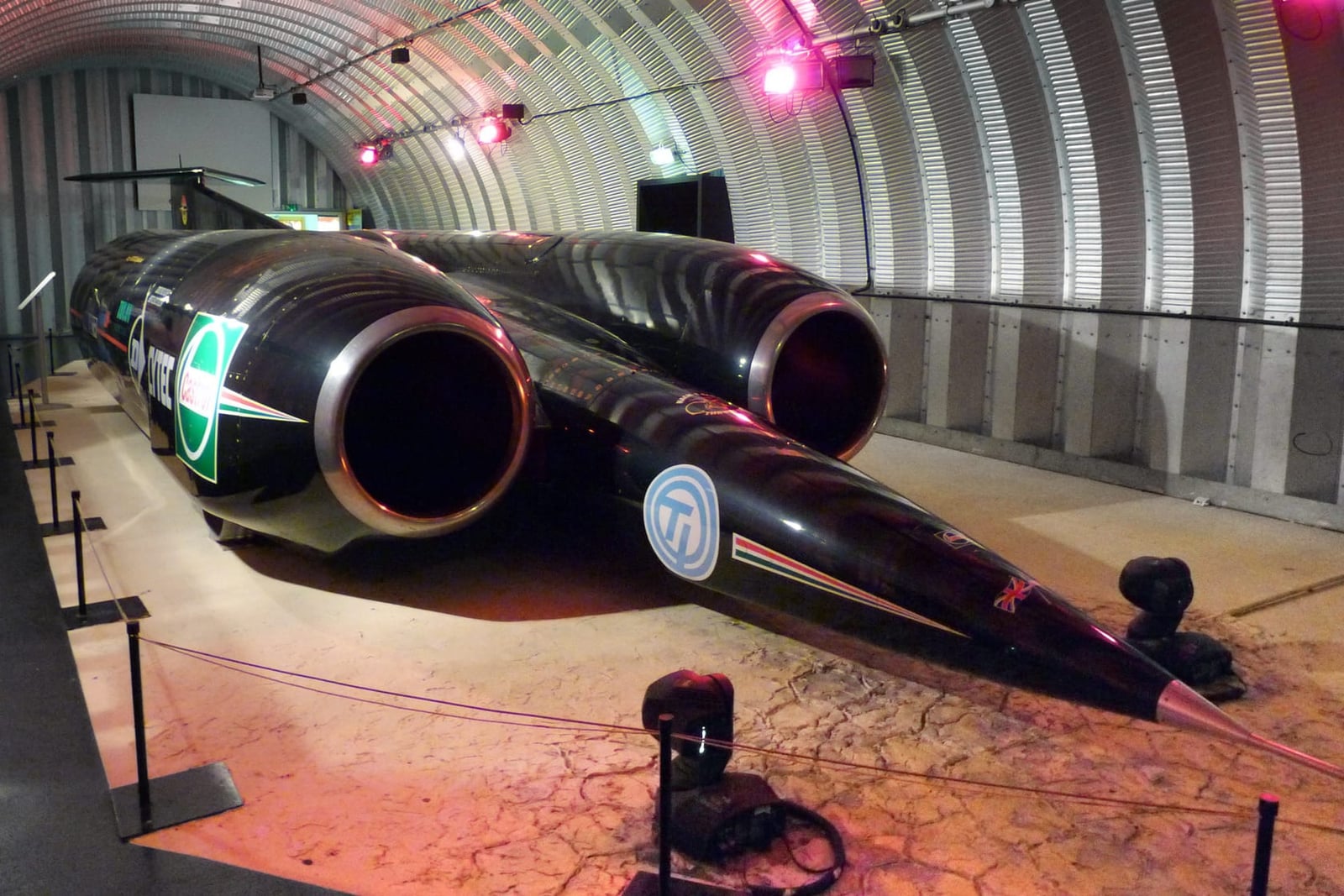 ThrustSSC, the black twin-jet supersonic record car, nose-on over a cracked-earth desert diorama in the Coventry Transport Museum