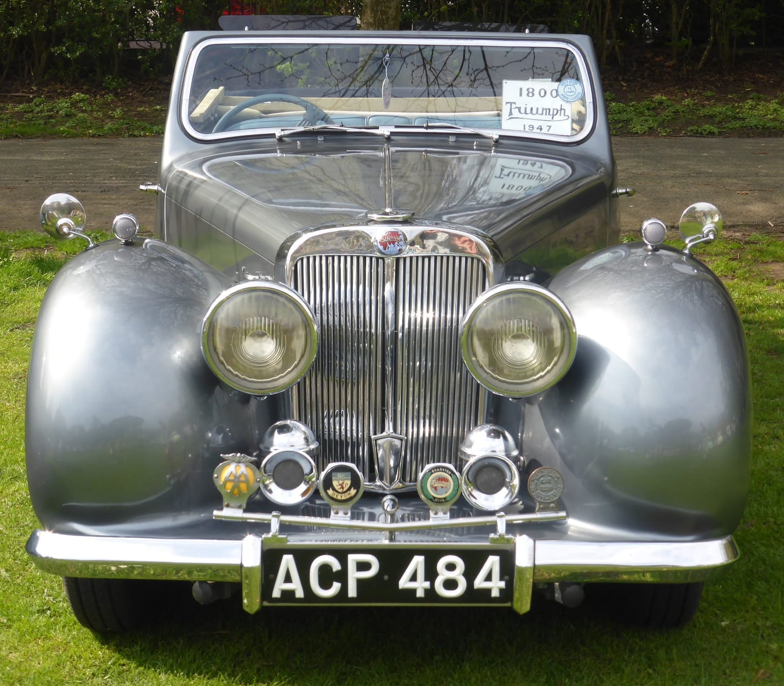 A silver-grey 1947 Triumph 1800 Roadster on grass at a classic car show, front view showing the wide grille and headlamps, UK registration ACP 484