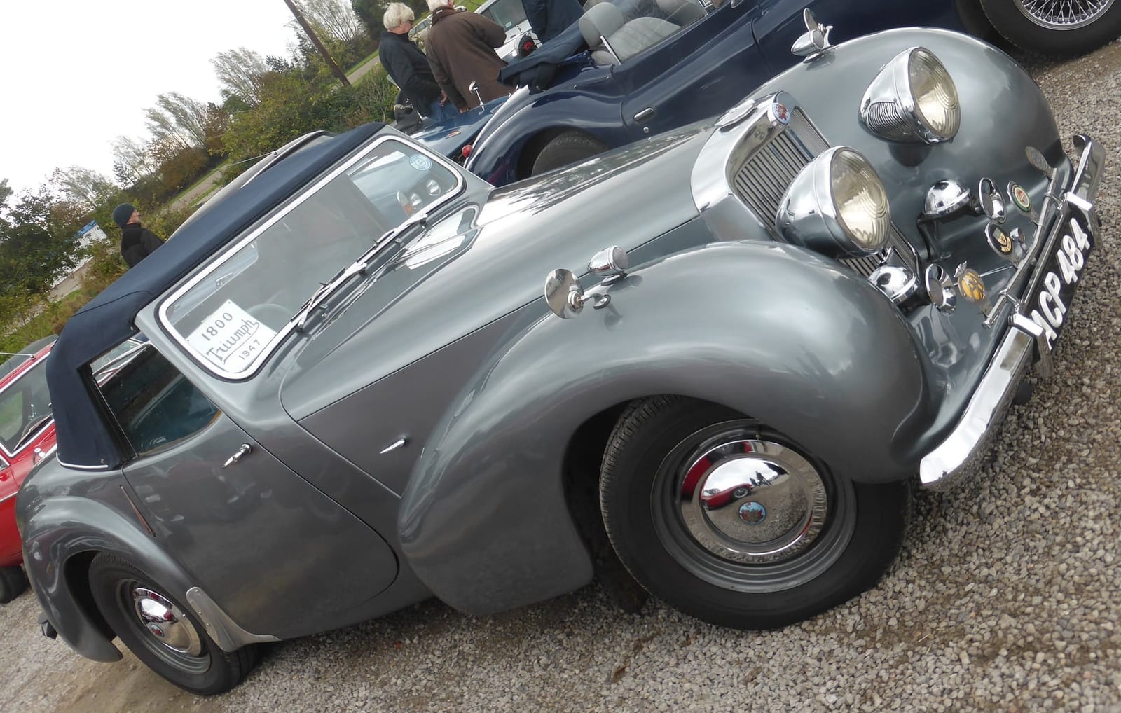 A grey Triumph 1800 Roadster with its hood raised, rear three-quarter view on gravel, UK registration ACP 484