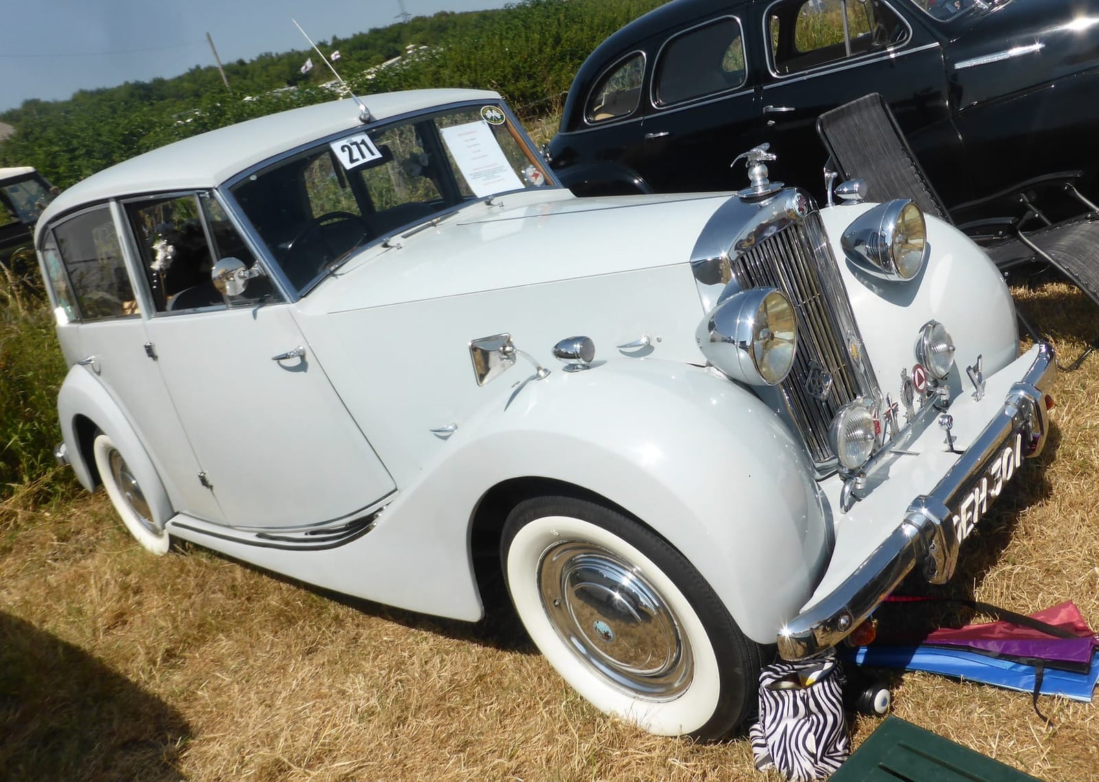 A white long-wheelbase Triumph Renown limousine on straw at a classic vehicle show, front three-quarter view