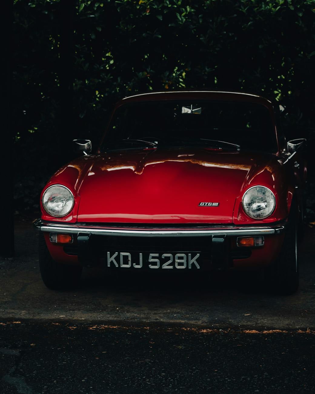 A red Triumph GT6, head-on front view against a dark hedge