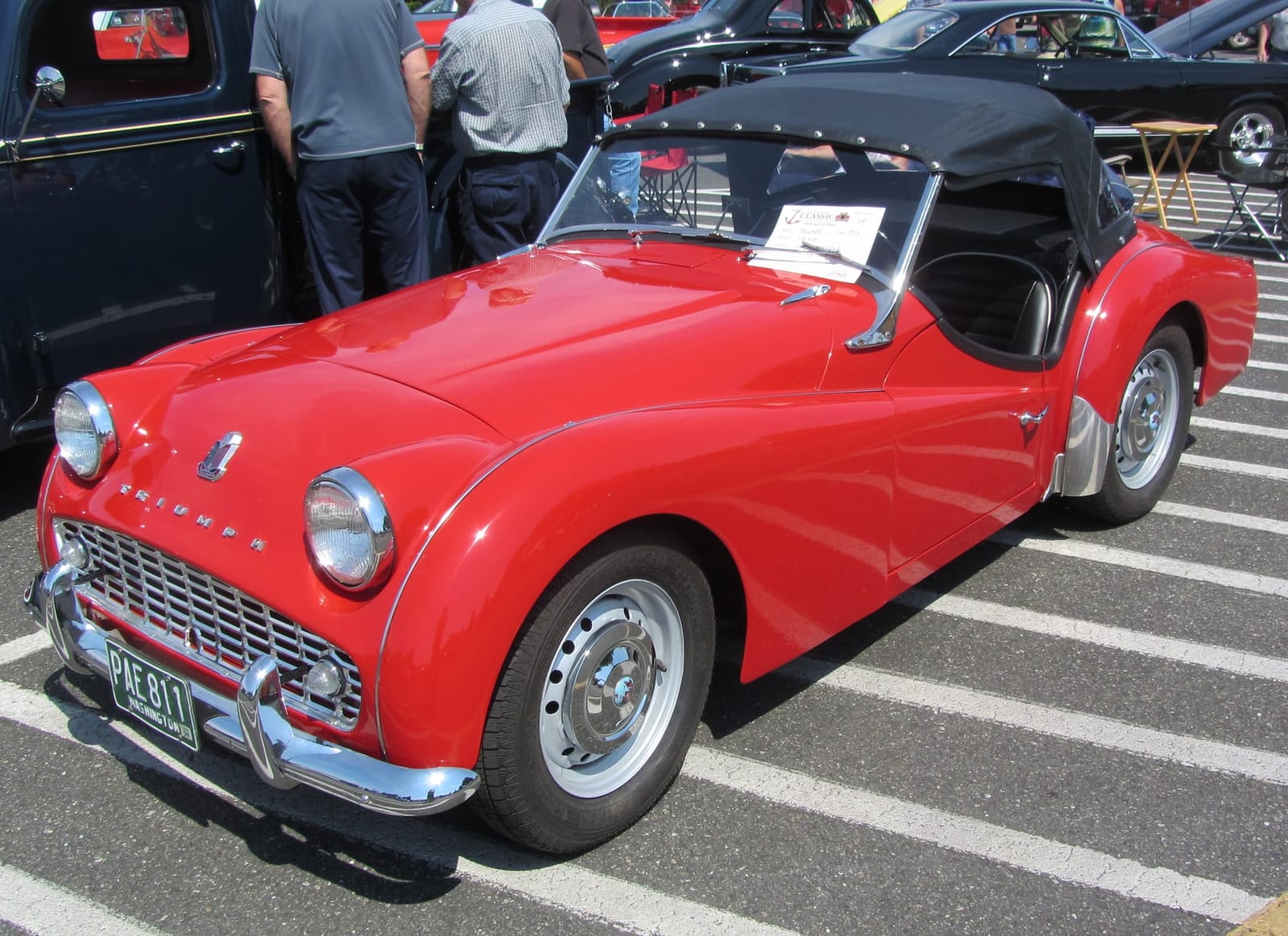 A red Triumph TR3 with the black hood raised, front three-quarter view at a classic-car show