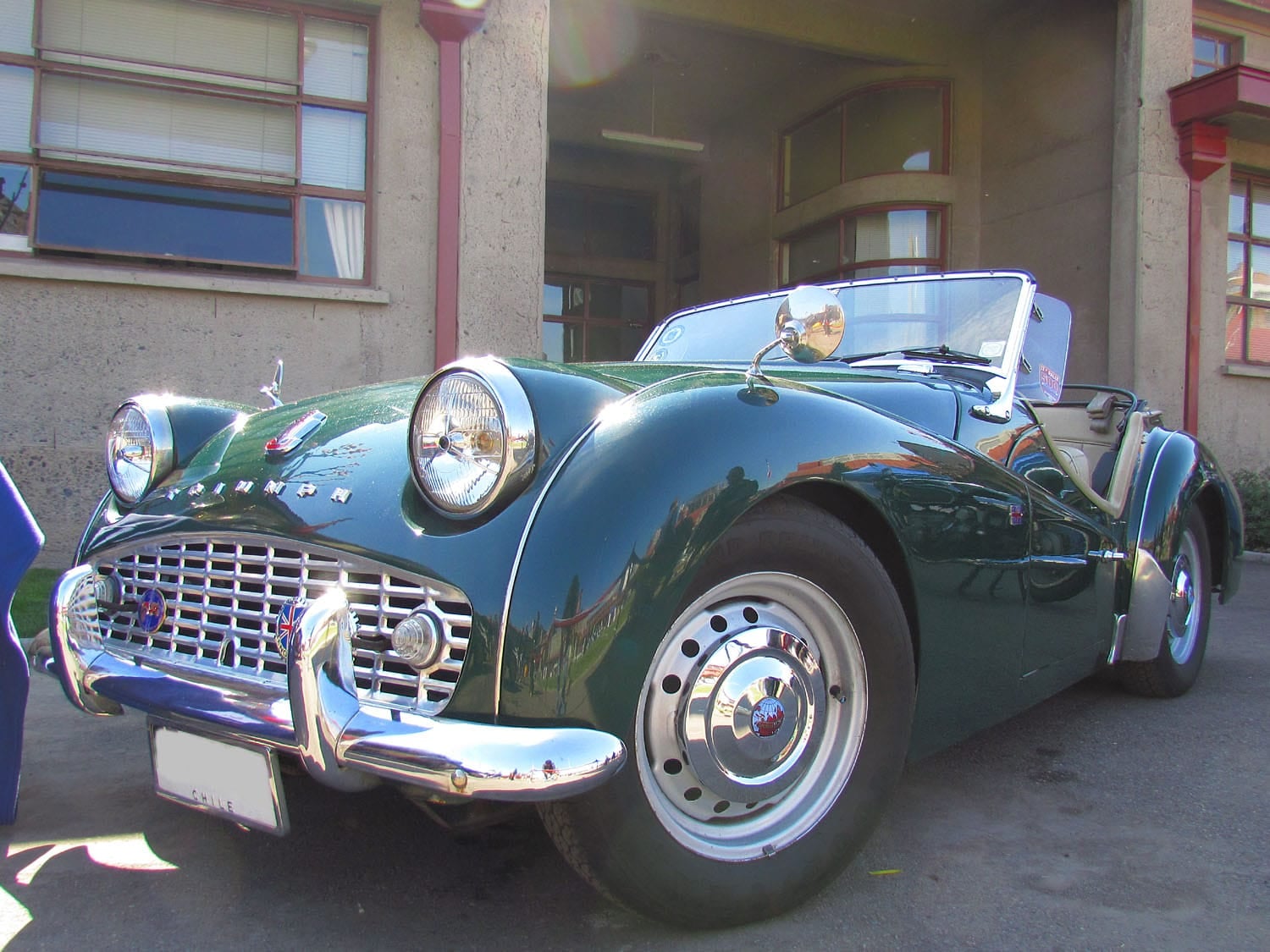 A dark green Triumph TR3A parked outside a building, front three-quarter view