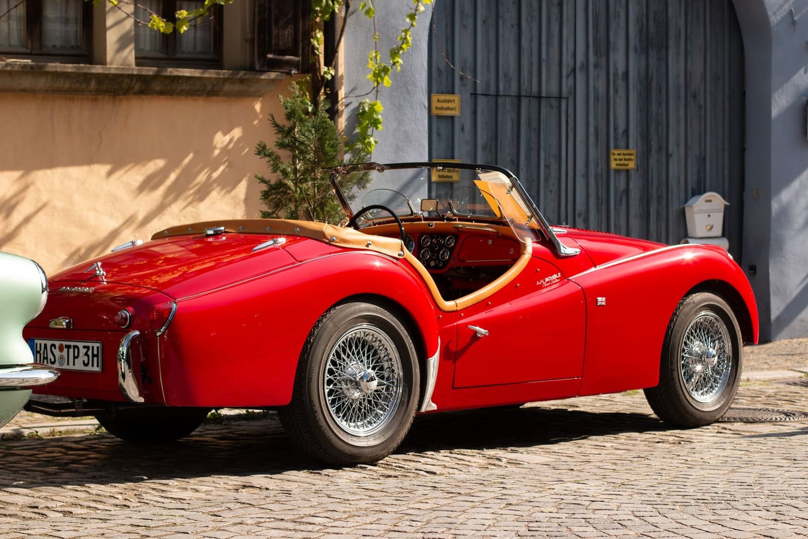 A red Triumph TR3 photographed from the rear three-quarter on a cobbled street, hood down