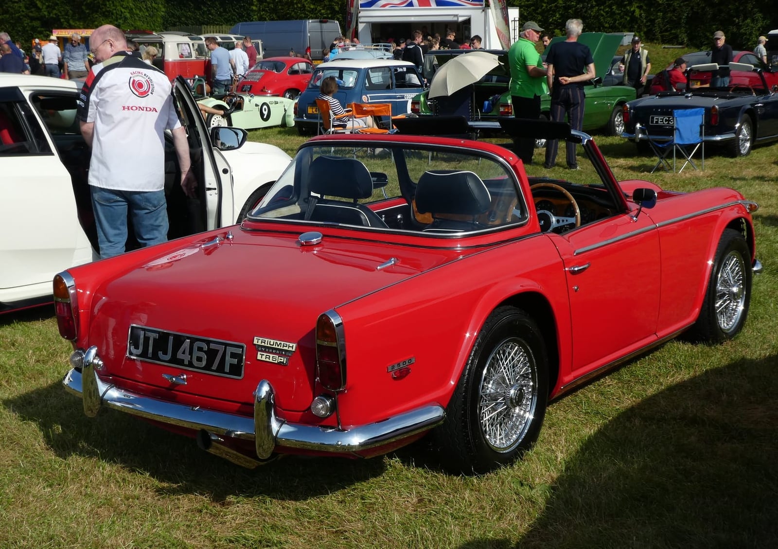 A red Triumph TR5 PI with the hood down at a show