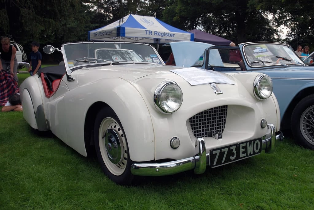 A white Triumph TR2 on a TR Register club stand at a classic car show, front three-quarter view, UK registration 773 EWO