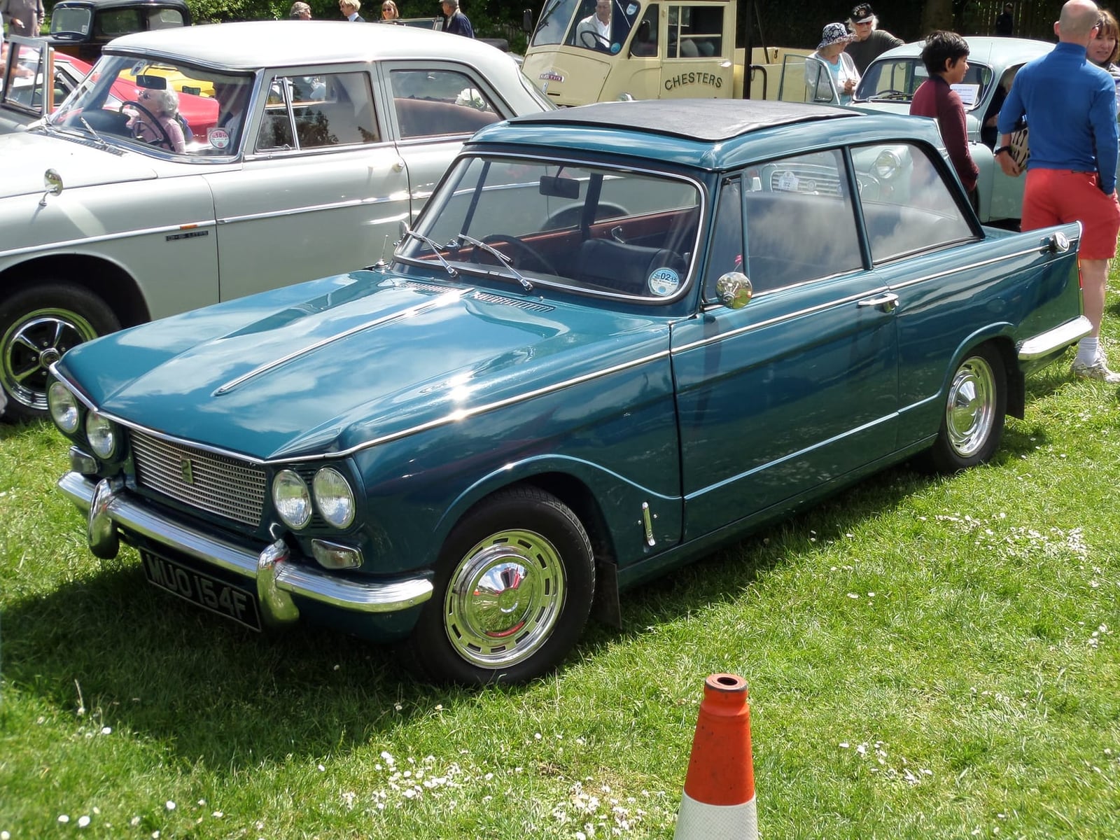 A teal 1967 Triumph Vitesse 2-litre on grass at a classic vehicle rally, front three-quarter view