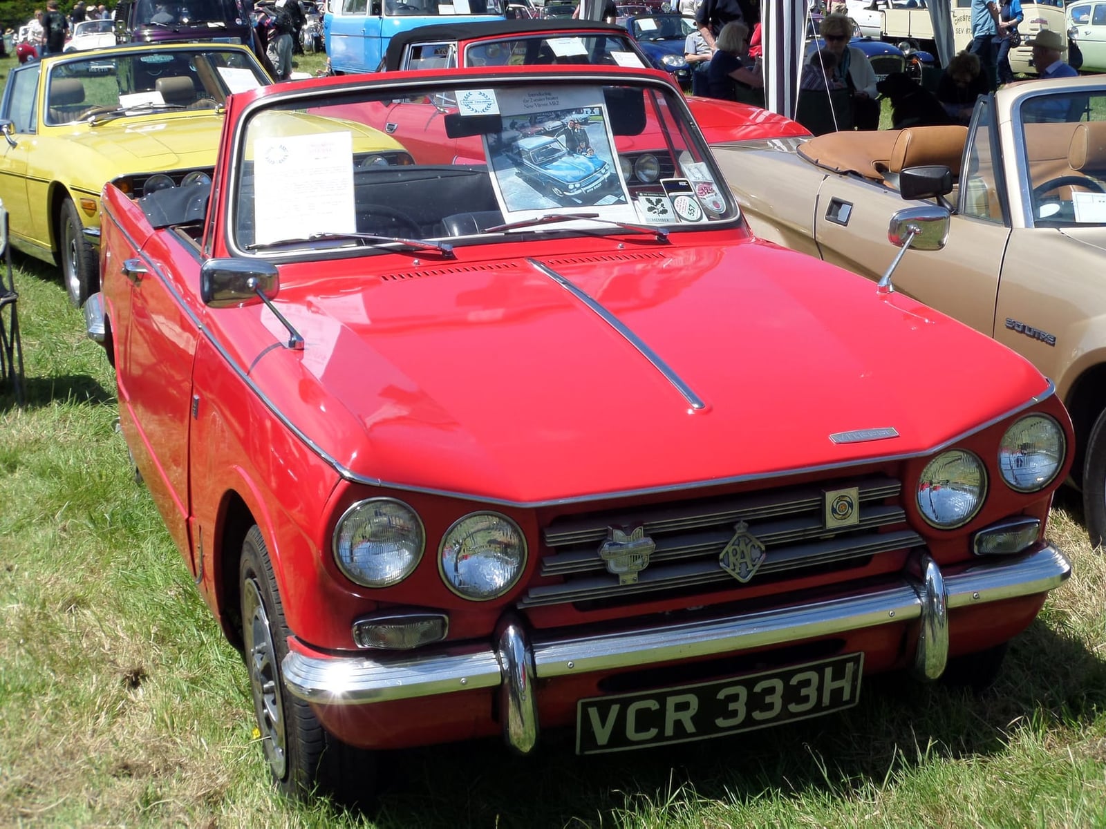 A red Triumph Vitesse 2-litre Mk2 convertible with the hood down at a classic car show, front three-quarter view, UK registration VCR 333H