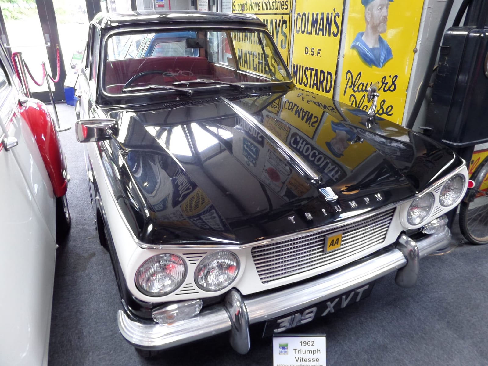 A white 1962 Triumph Vitesse 6 on museum display in front of period enamel advertising signs